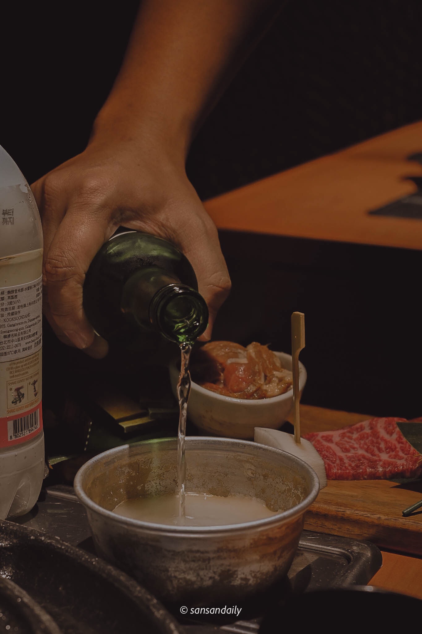 一個人將真露燒酎倒入在桌上的鋁碗