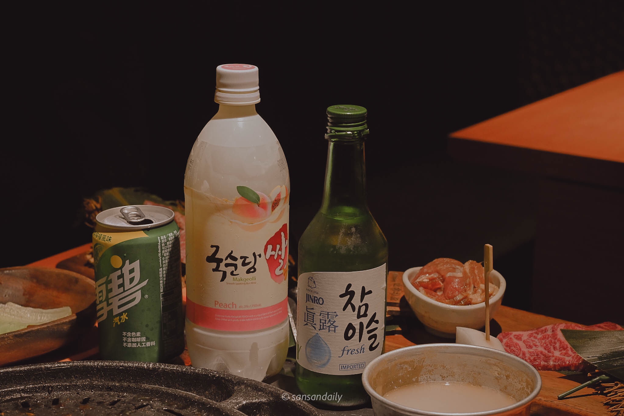 桌上擺著一瓶雪碧、水蜜桃口味馬格利以及真露燒酎