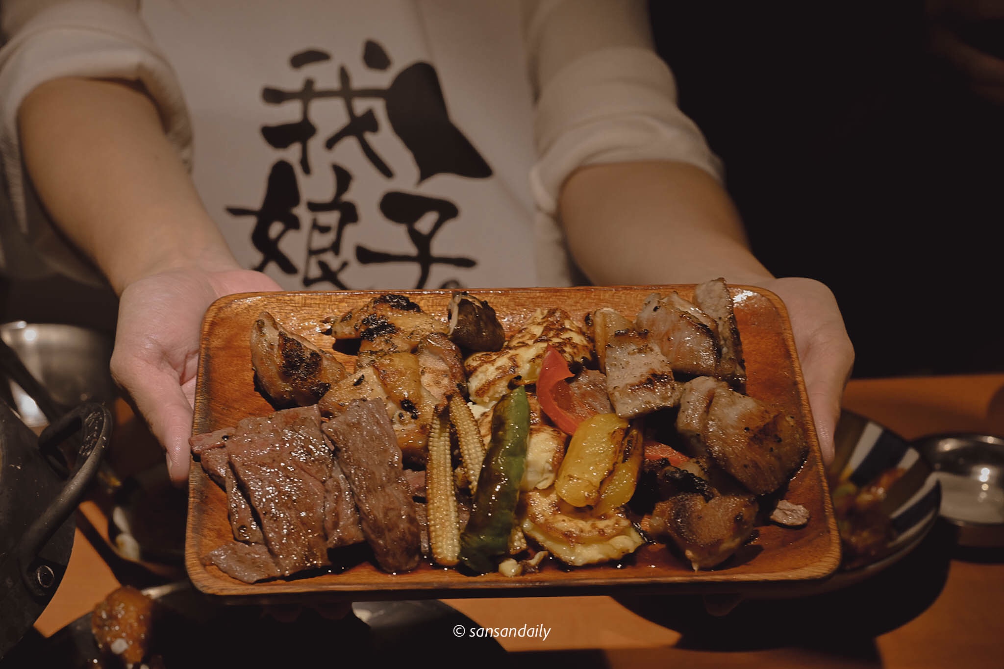 一位美女端著裝有燒烤和烤蔬菜的木盤