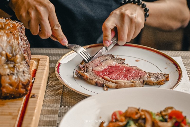 一位男子拿刀叉切著Mr.Tom爐烤肋眼牛排