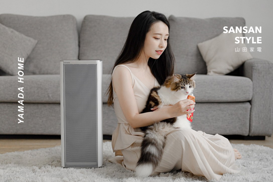 女孩坐在客廳地板上 抱著一隻貓 左側擺著一台空氣清淨機