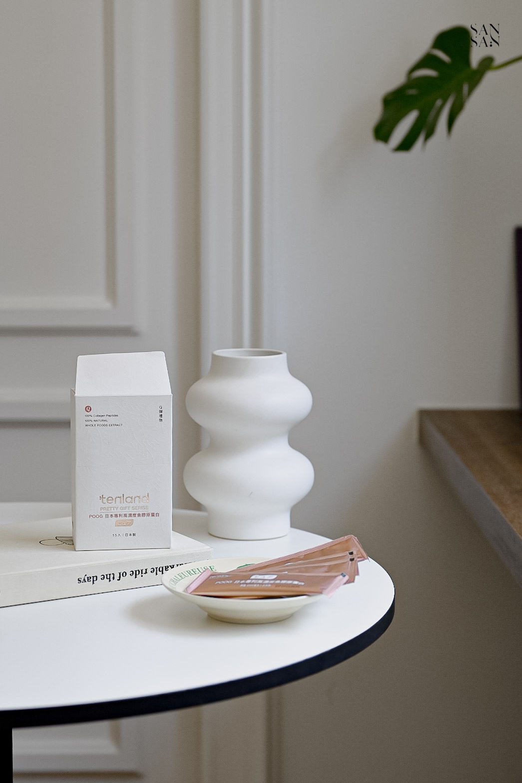 白色圓桌上放著白色外盒、一個盤子裡面放著數包膠原蛋白、一個造型純白花瓶