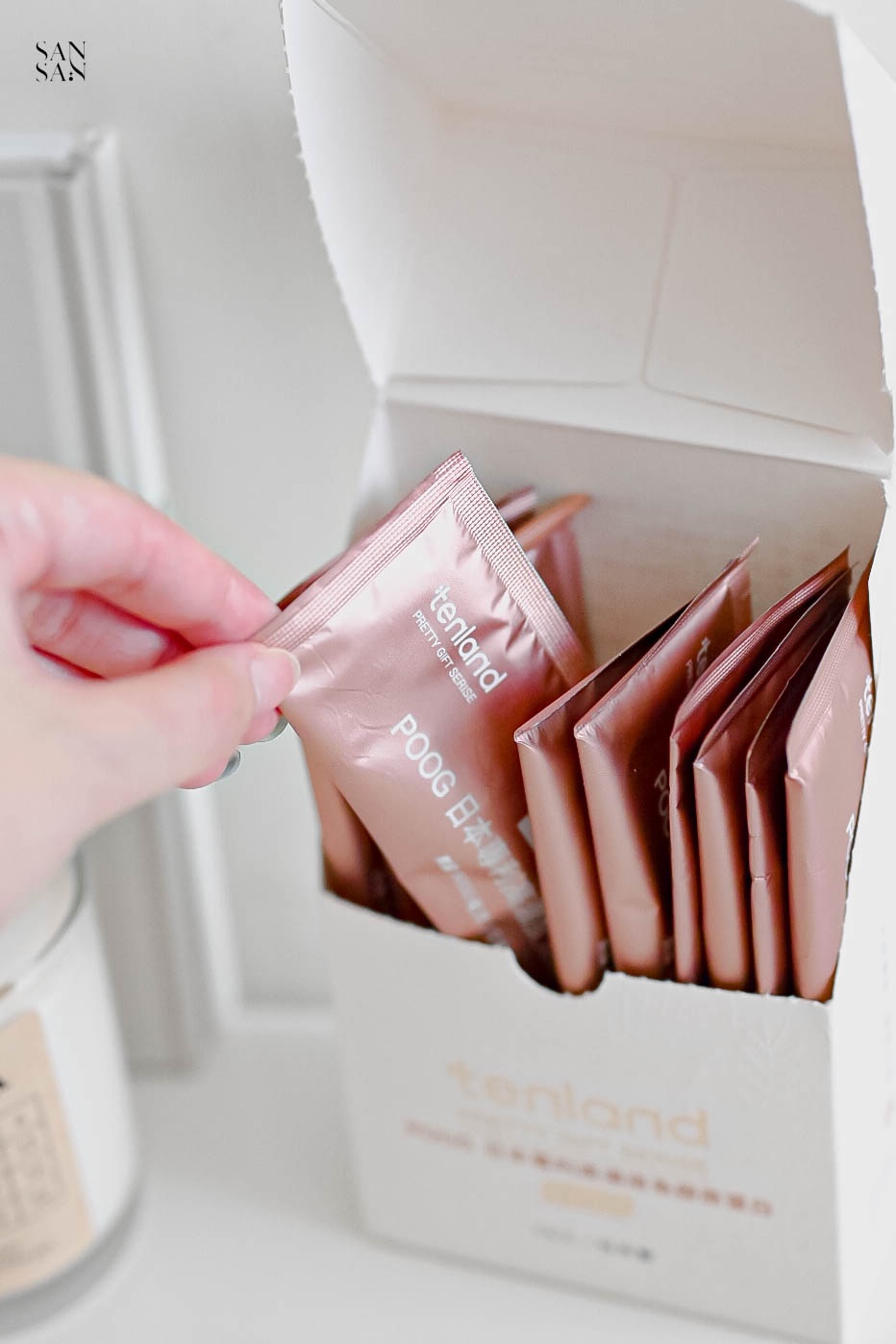 一隻手從打開的盒中取出一包粉橘色的天嵐里物單包裝膠原蛋白粉