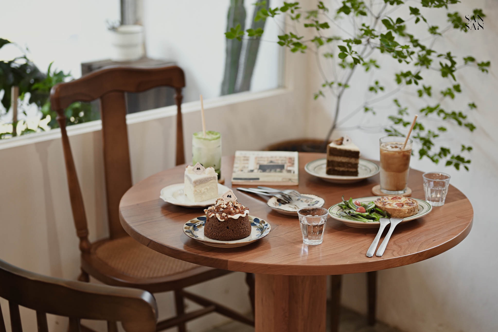 圓木桌上擺滿餐點 甜點和飲品 牆邊有綠色植栽