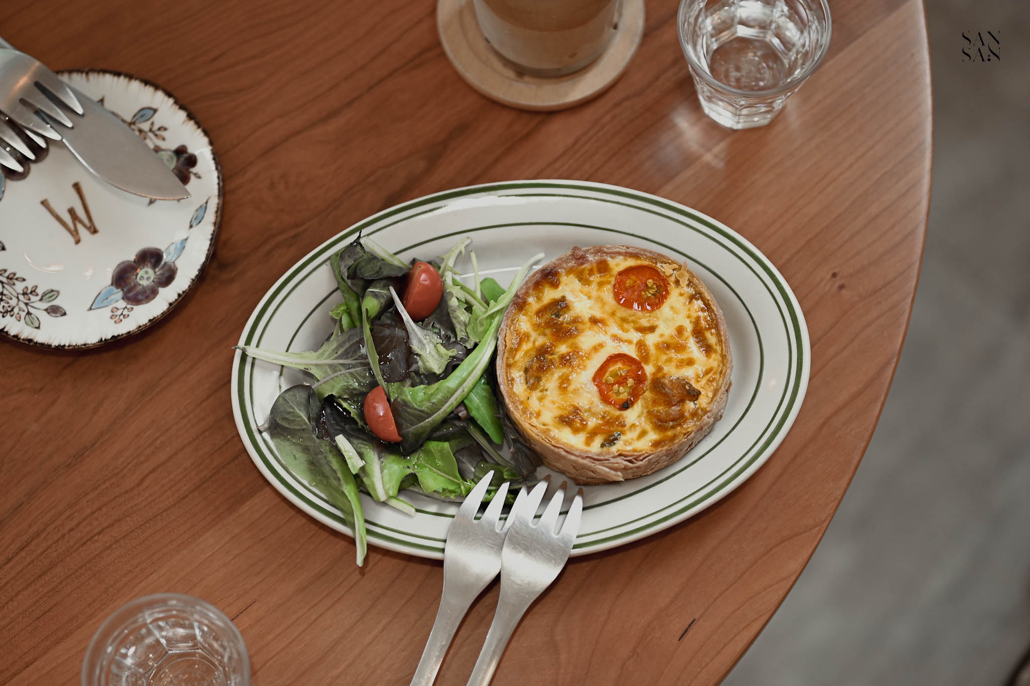 桌上放一個盤子  其中有鹹派和生菜沙拉 旁邊友叉子和水杯