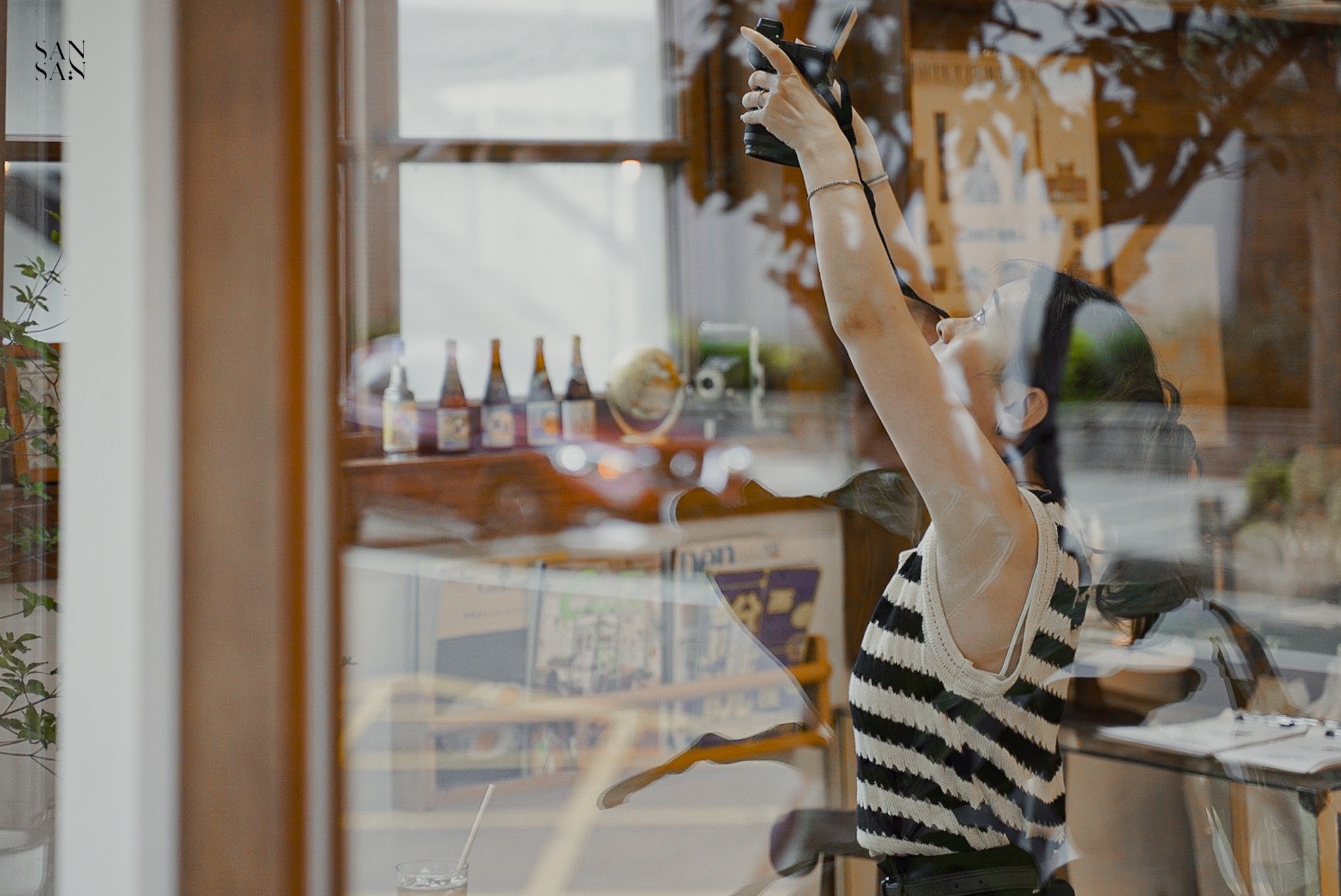 透過玻璃窗向內看 一位女子高舉相機拍攝中