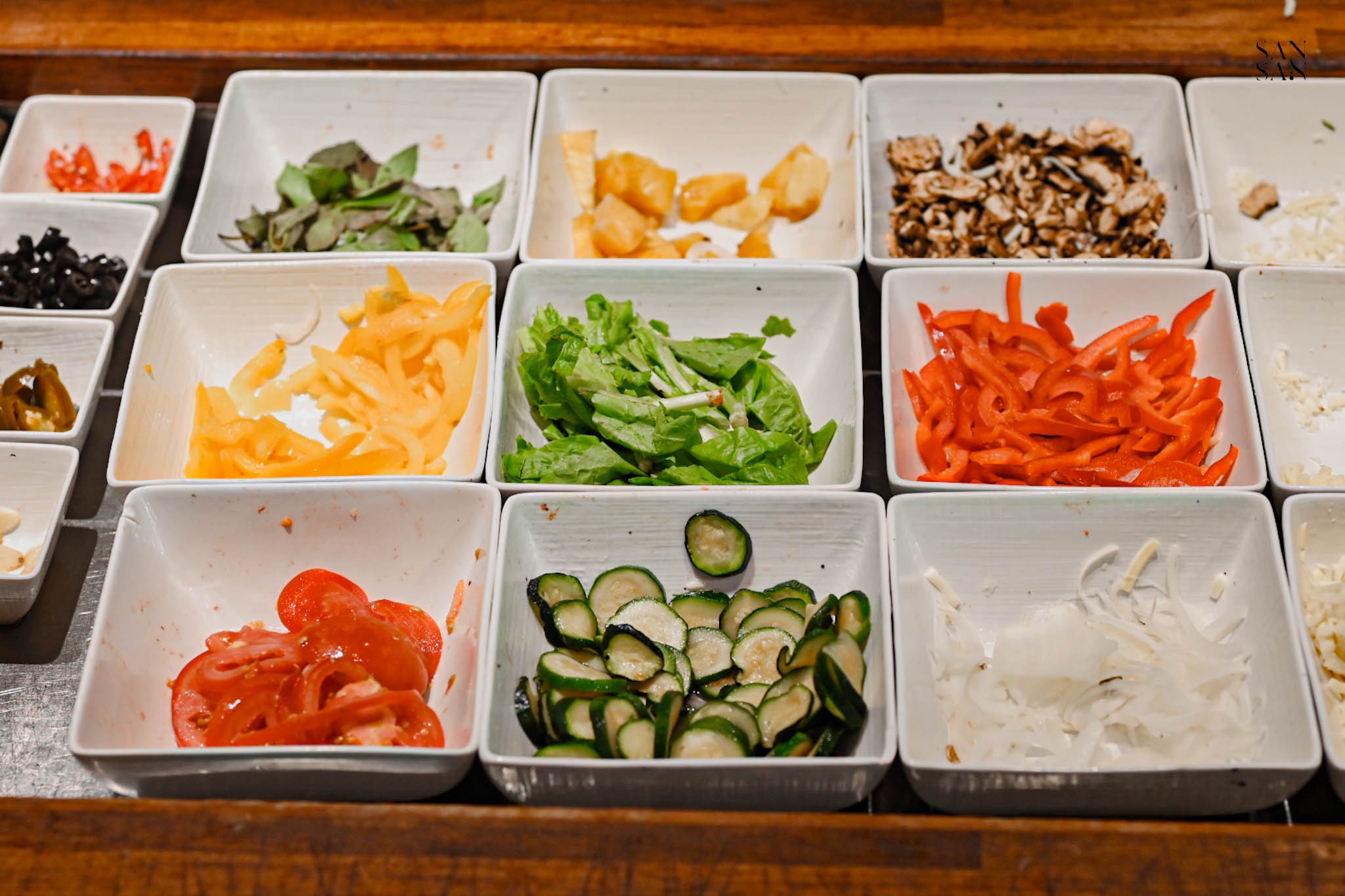 披薩DIY的食材區：彩椒、生菜、番茄、洋蔥、蘑菇、羅勒葉、櫛瓜和鳳梨等