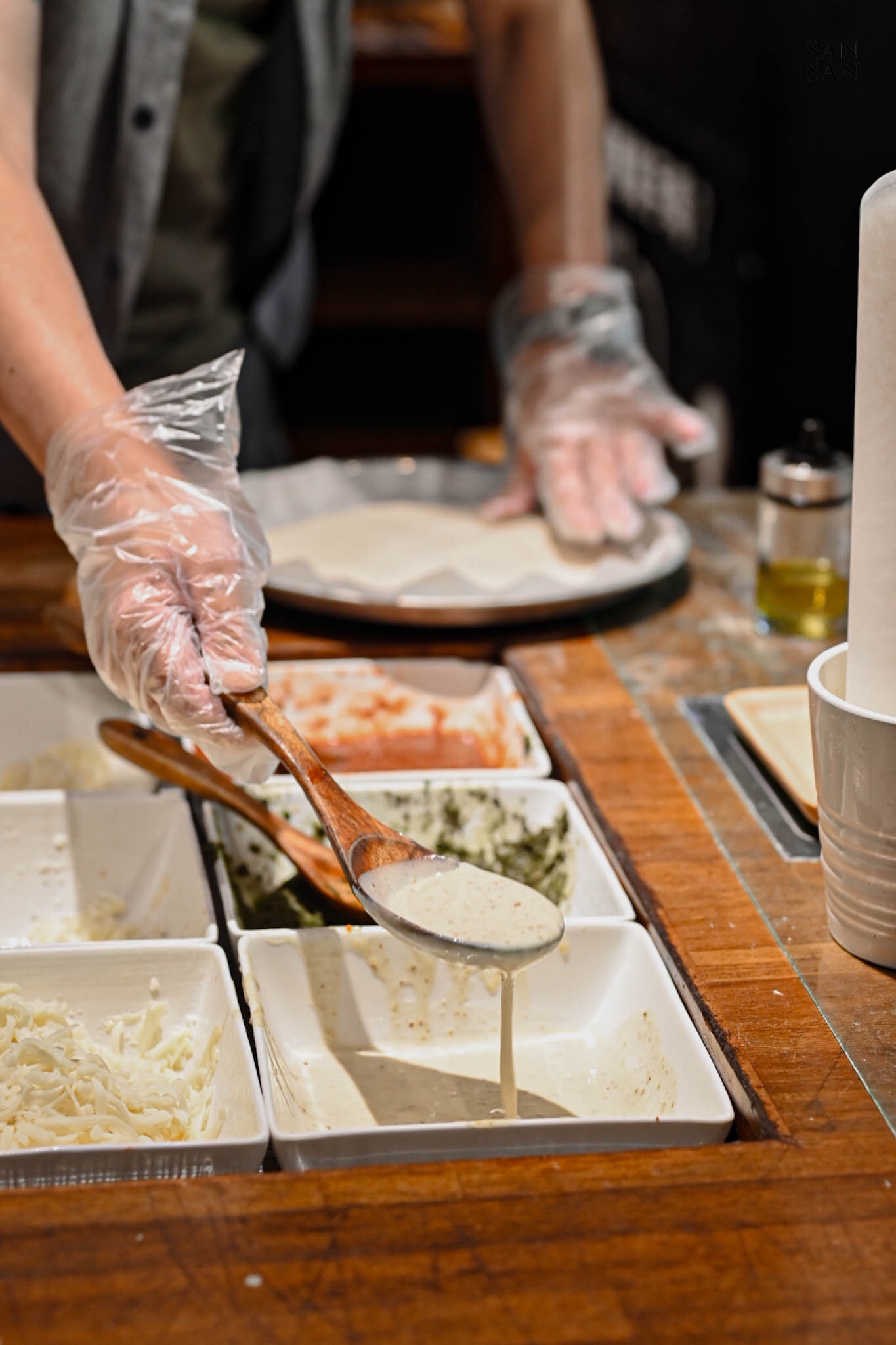 一支戴手套的手持木湯匙舀白醬畫面