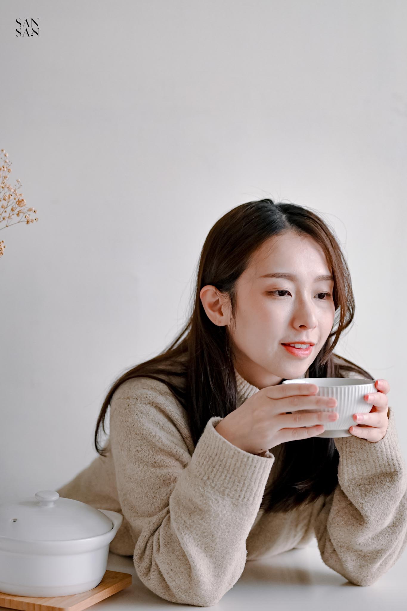 女人手肘撐在桌面上 雙手端著碗微笑