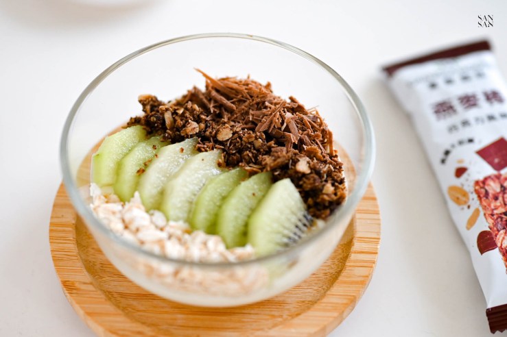 用玻璃碗裝的優格水果碗，優格上整齊地擺放奇異果、燕麥以及巧克力碎