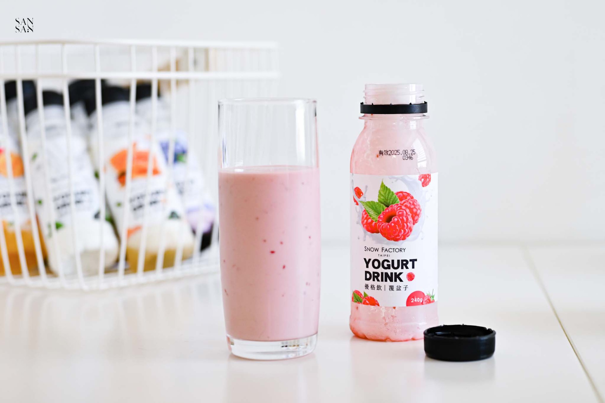 裝上有一瓶空的覆盆子優格飲，旁邊是一杯倒滿粉嫩色優格飲的玻璃杯