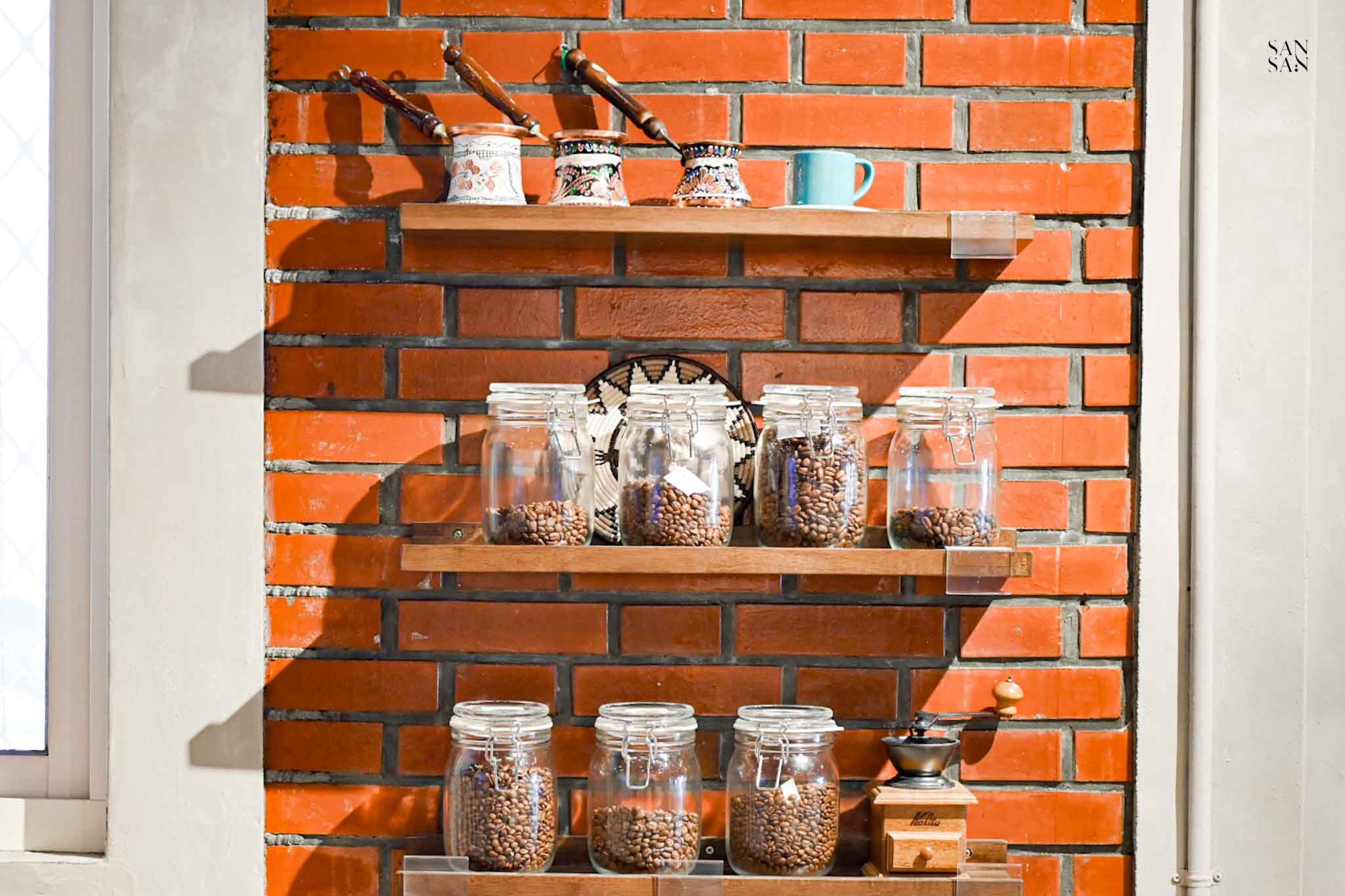 紅磚牆上釘了木製層架，擺放整齊的咖啡罐以及女主人收藏的土耳其咖啡壺