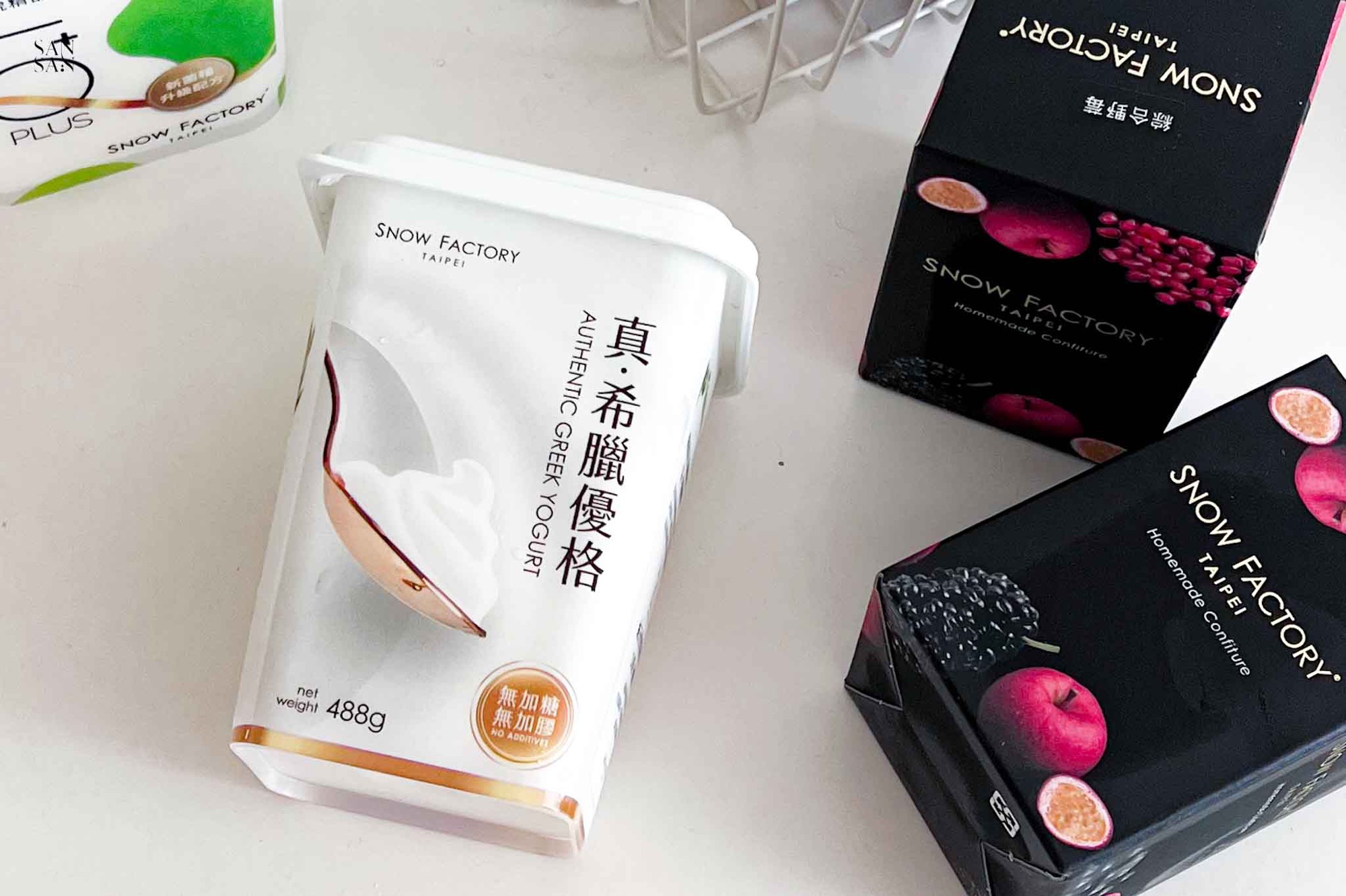 一罐雪坊 真希臘優格擺放在桌上，旁邊有兩盒法式果醬