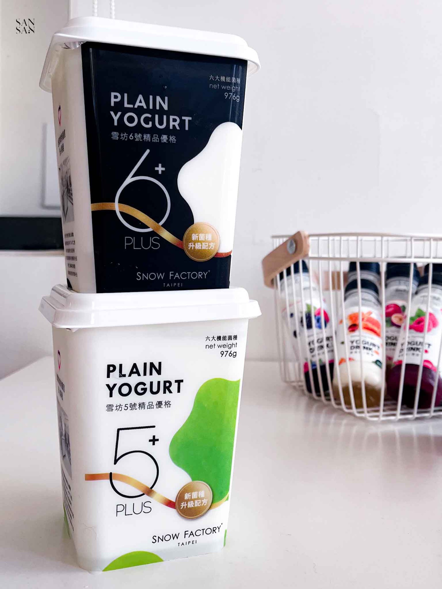 1盒雪坊6號優格擺放在1盒5號精品優格上面，背景是一籃優格飲